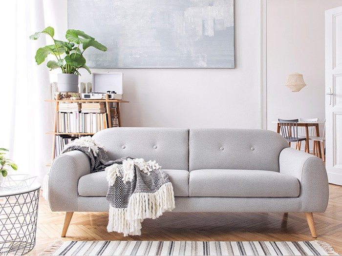 Petit salon avec un petit canapé gris aux pieds apparents et une couverture drapée sur l’accoudoir et l’assise.