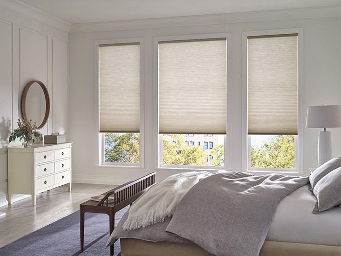 Chambre à coucher lumineuse dont les grandes fenêtres sont équipées de stores en nid d’abeilles DuetteMD.